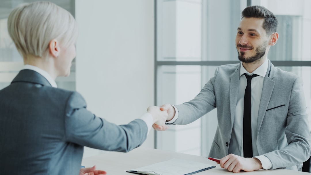 Two professionals shaking hands across a desk in an office
