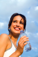 Woman smiling holding water bottle with clouds in the background