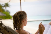 woman relaxing on the beach reading and holding a cigarette